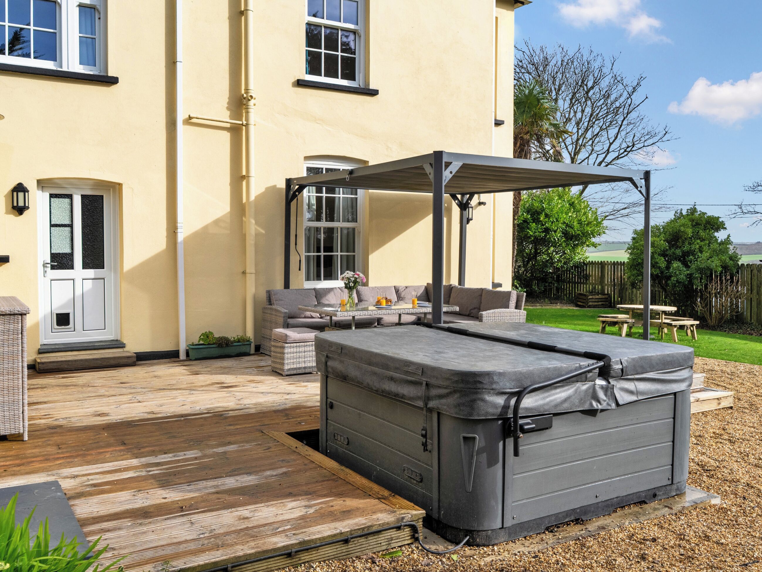 Un patio con mobiliario exterior, una zona de estar cubierta y un jacuzzi.