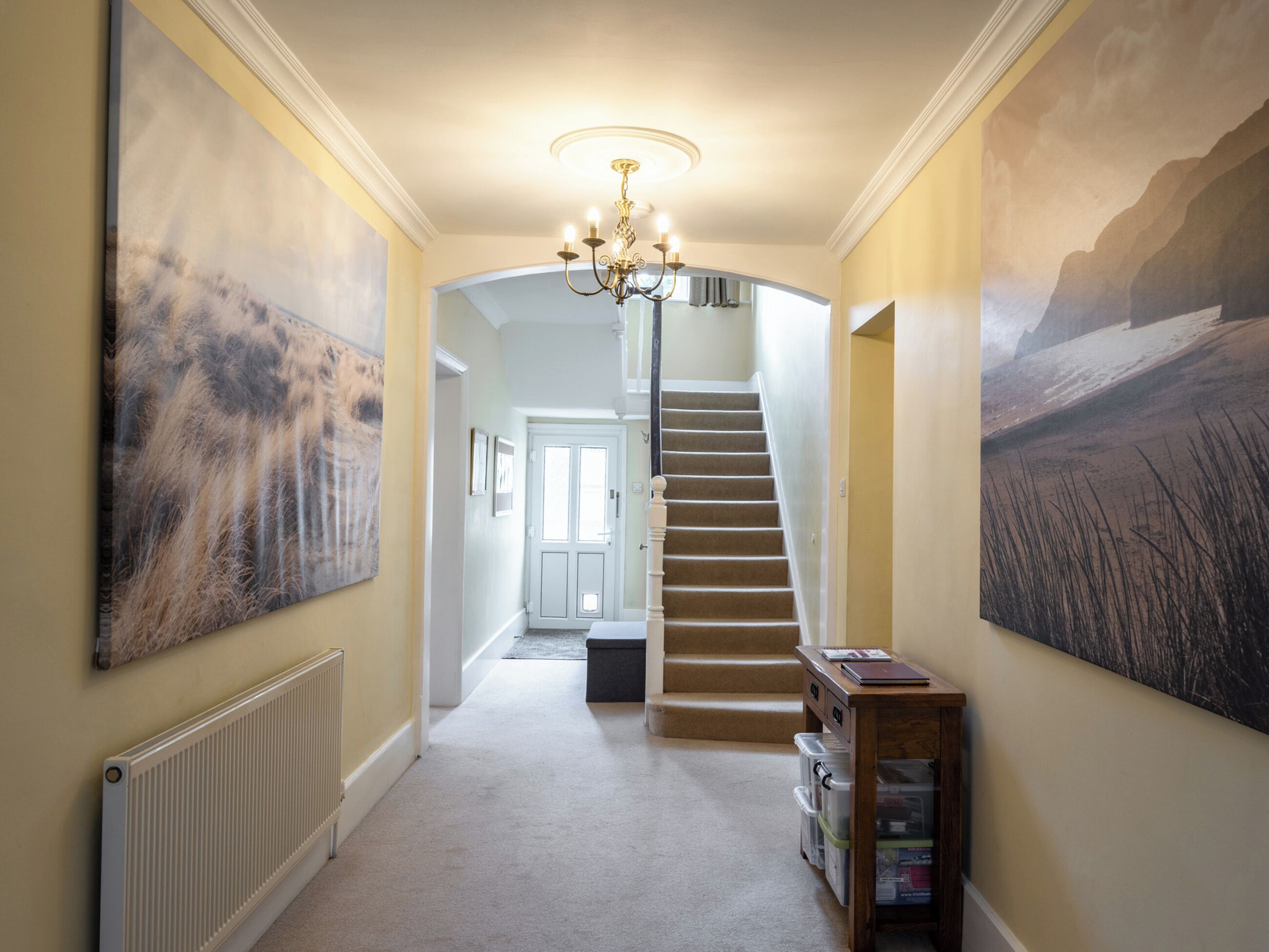 A hallway with a carpeted floor, a staircase, and a chandelier.
