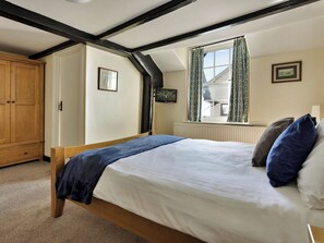 Ein Schlafzimmer mit Bett, Kleiderschrank, Fenster mit Vorhängen und Heizkörper.