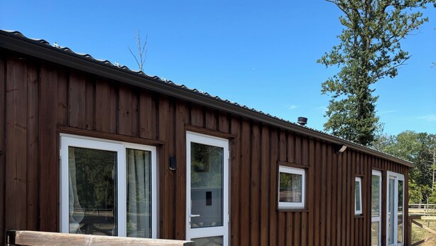 A wooden building with large windows and a deck. - Equi Lodge Jacuzzi in the heart of the forest near Disney (La Houssaye-en-Brie)