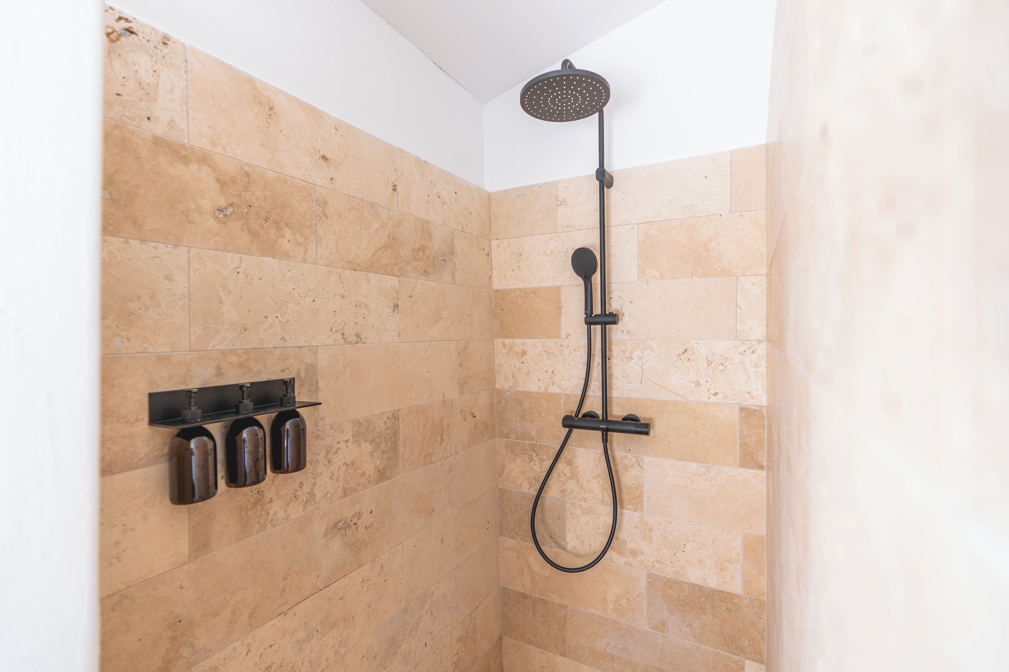 A shower with a handheld showerhead and a wall-mounted control panel.