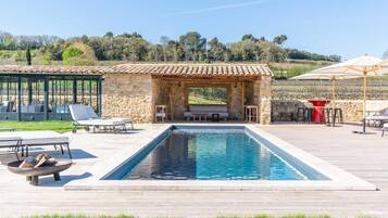A swimming pool with lounge chairs and a pergola, surrounded by stone walls and a vineyard in the background.