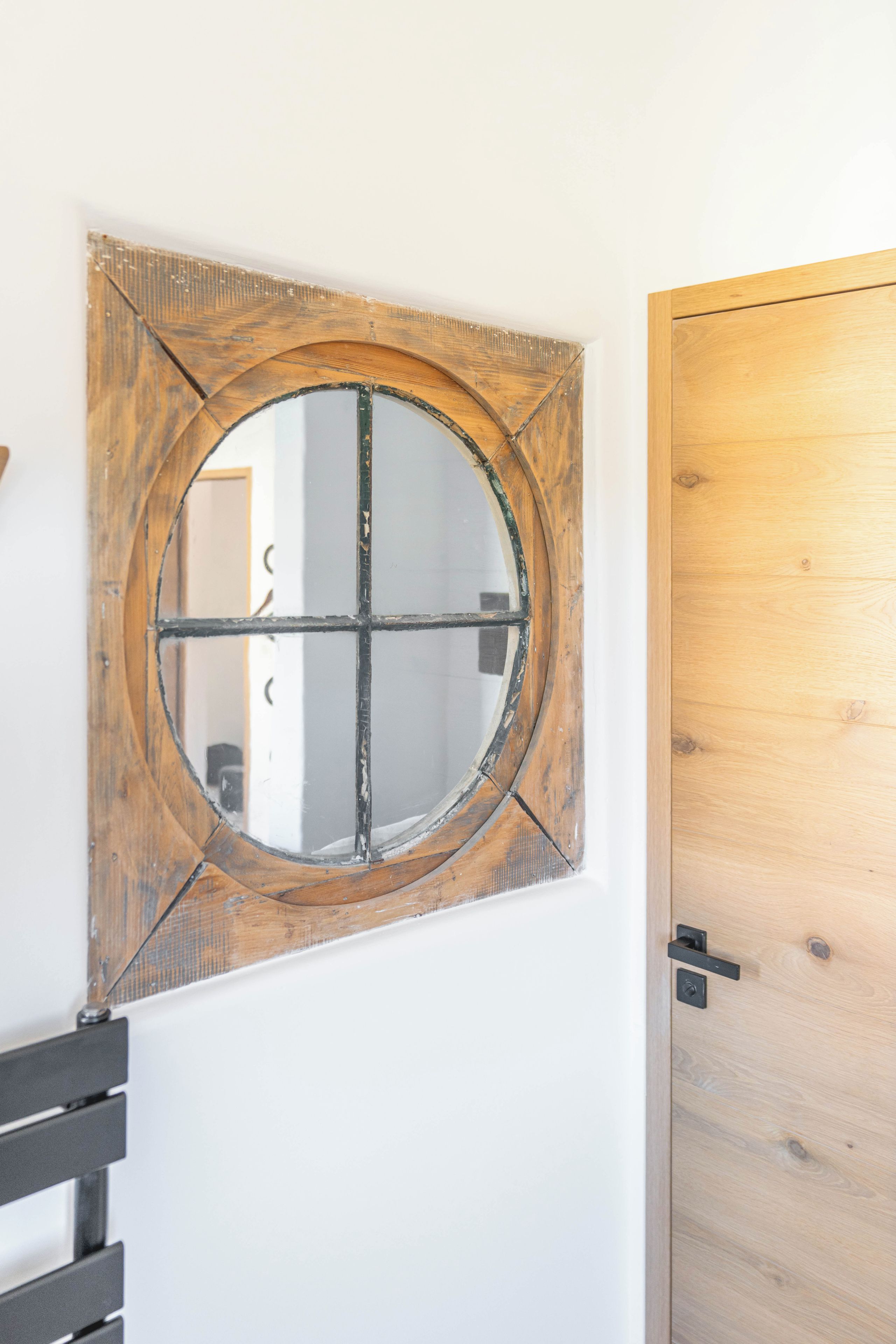 A wooden-framed window with a grid design, a white wall, and a wooden door.