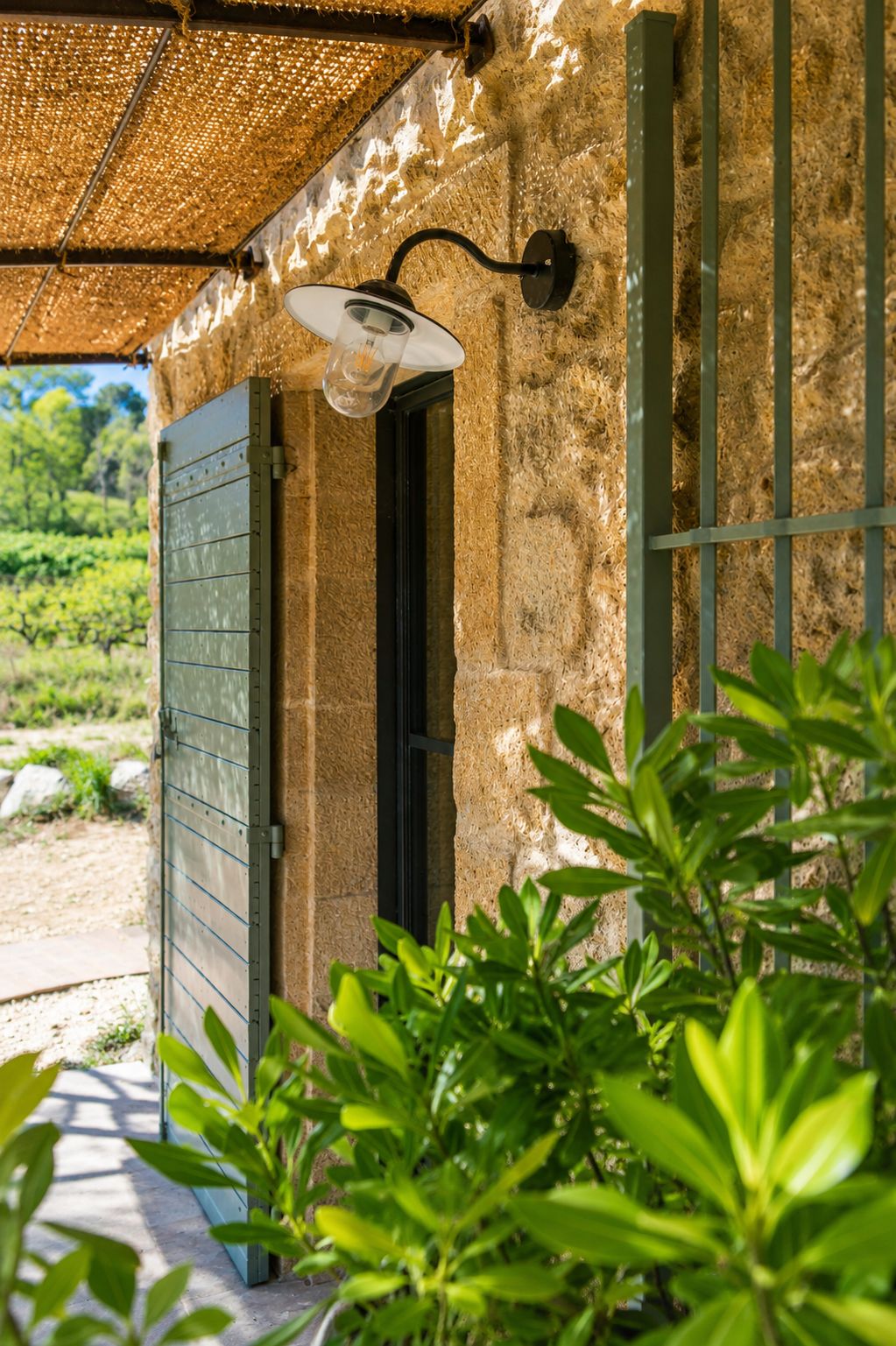 A doorway with a metal gate, a wall-mounted light fixture, and a view of a garden with greenery.