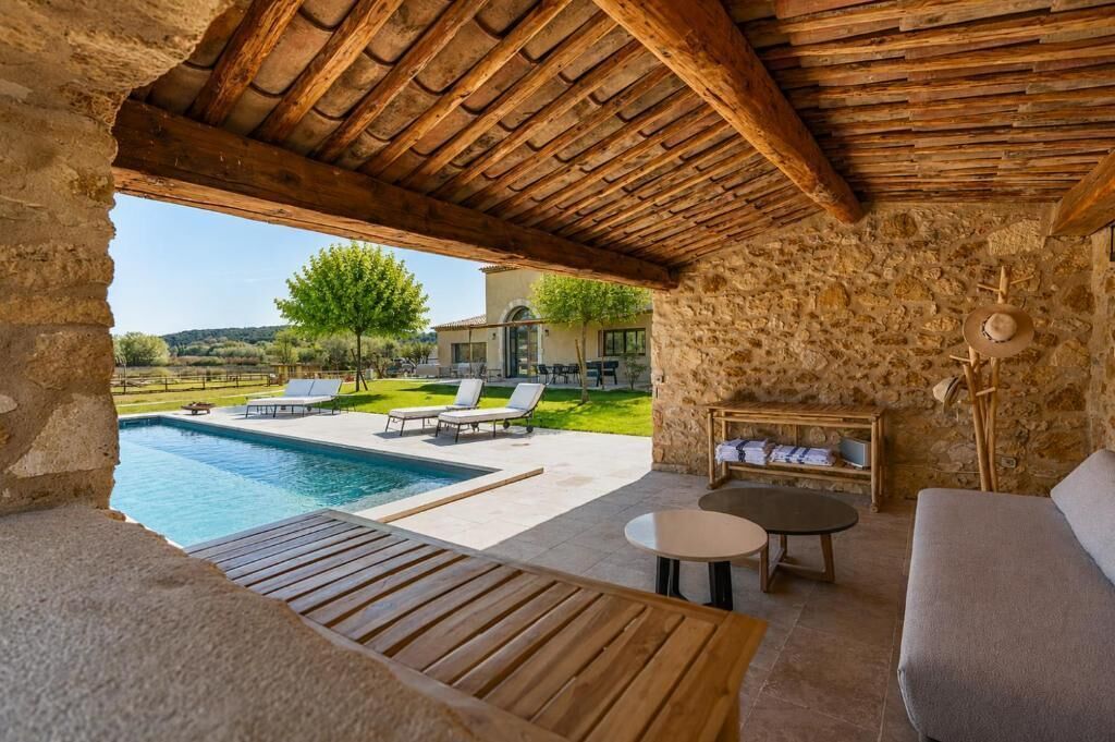 A stone-walled room with a wooden ceiling, a pool, and outdoor seating.
