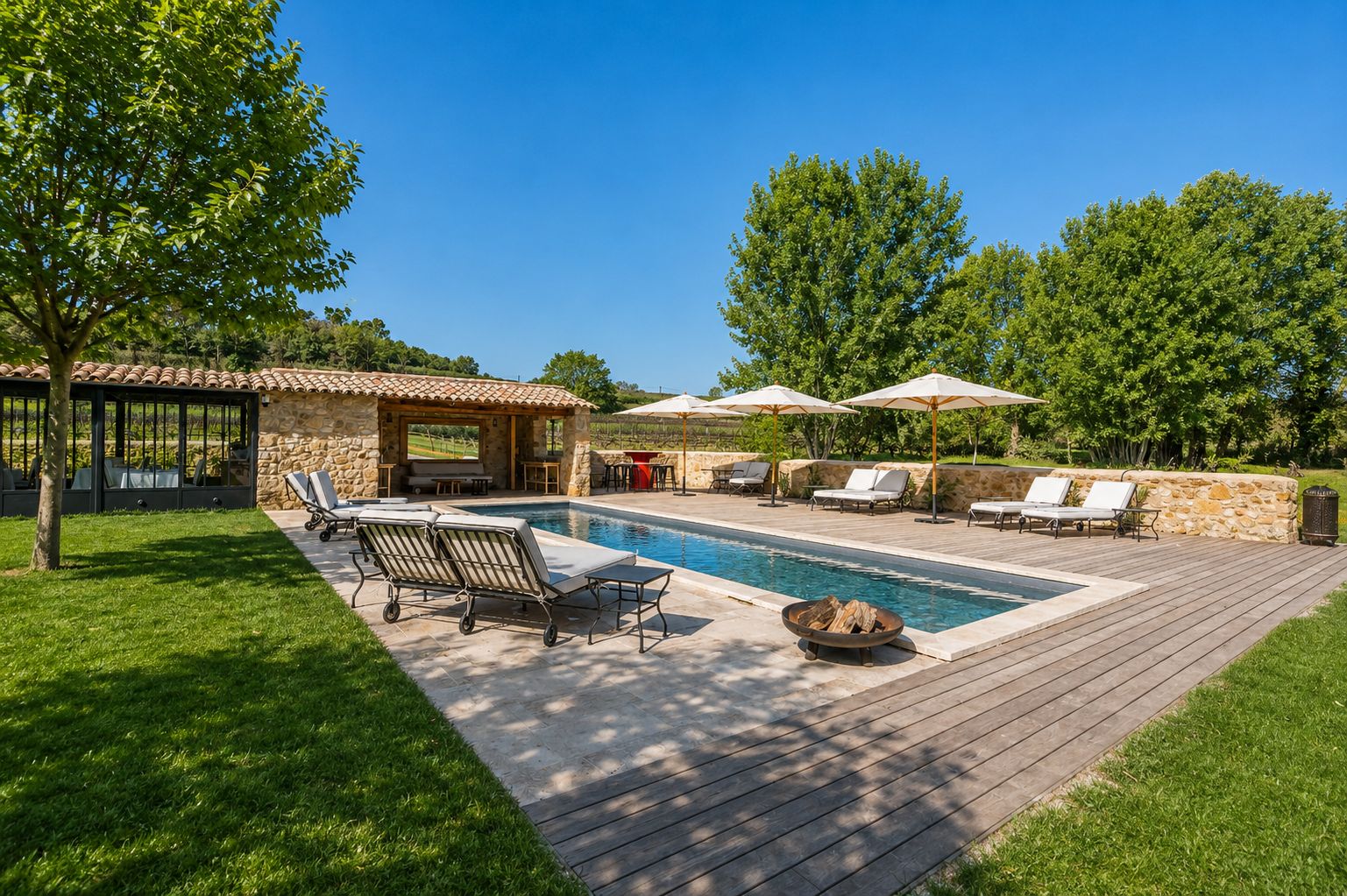 Un espace piscine doté de chaises longues et de parasols, entouré de murs en pierre et de verdure.