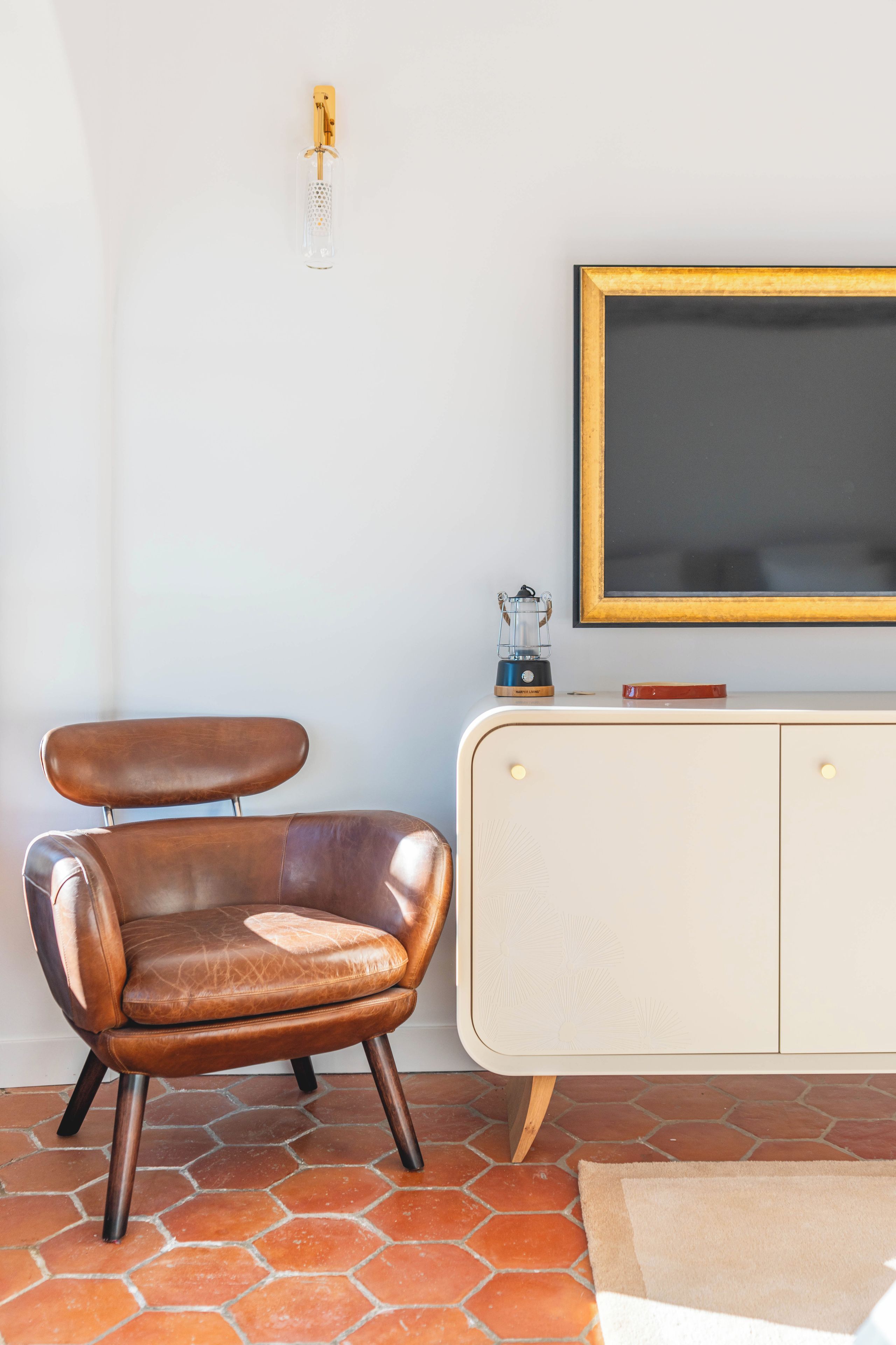 Une pièce avec un fauteuil en cuir marron, une armoire blanche dotée d’un tableau noir et un sol carrelé.