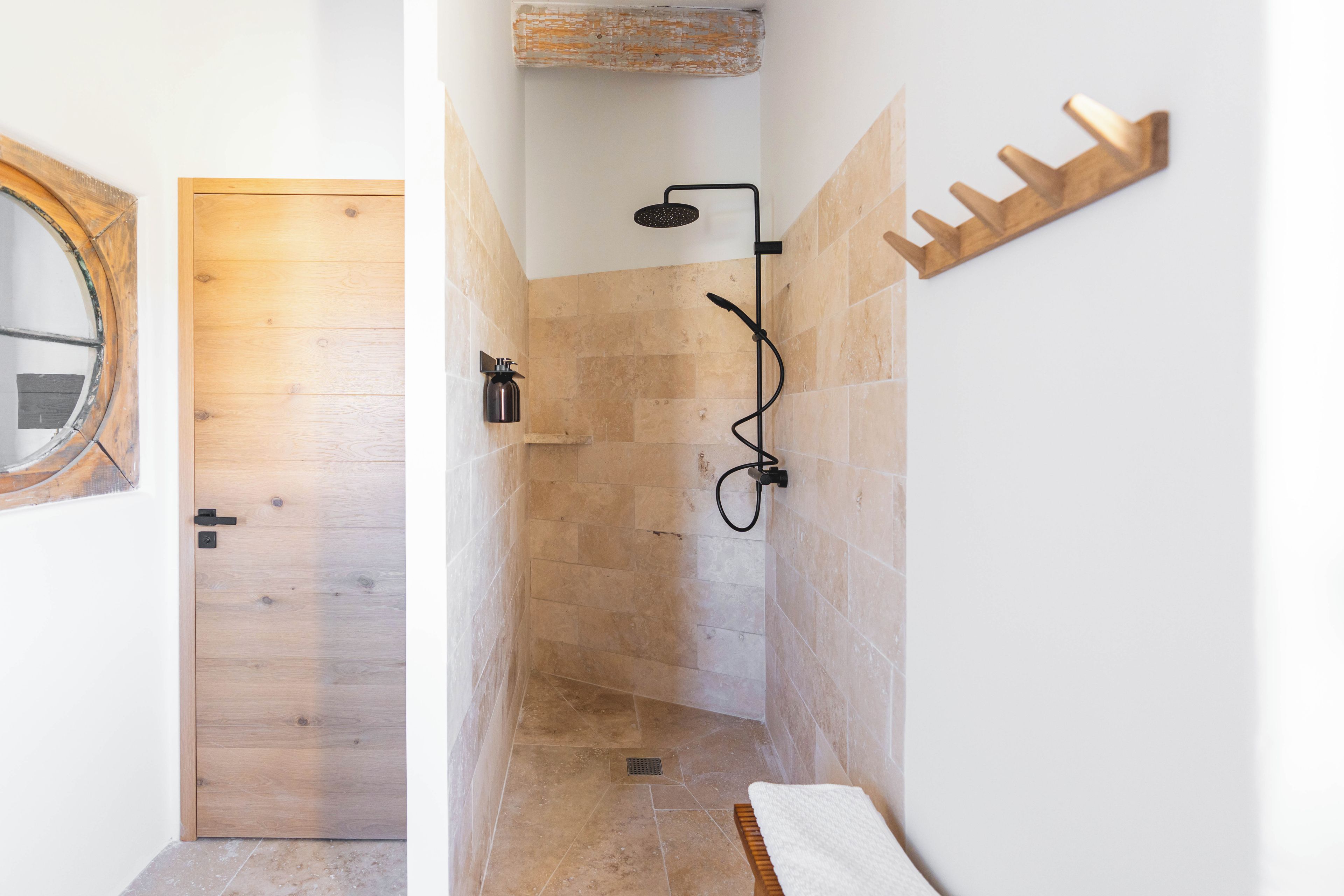 A bathroom with a wooden door, a shower with a handheld showerhead, and a towel rack.