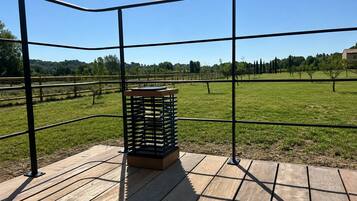Eine Holzterrasse mit Metallgeländer, die auf ein Wiesfeld mit Bäumen und ein Gebäude in der Ferne blickt.
