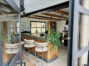 A modern kitchen with a bar area, wooden beams, and a large window.