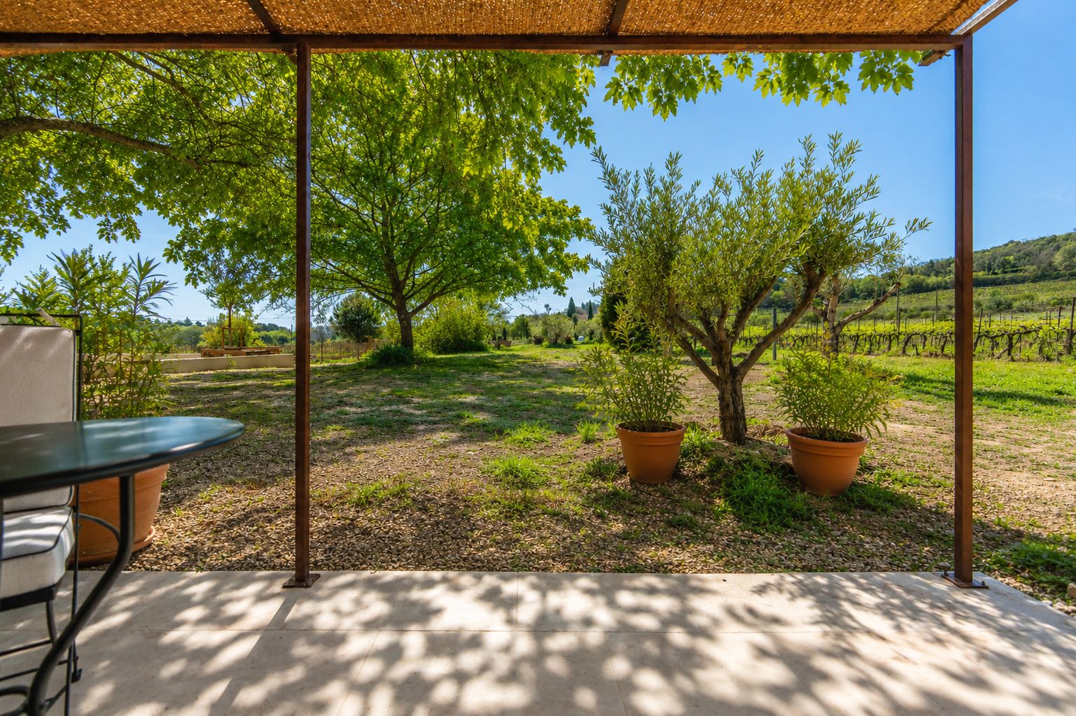 An outdoor patio with a table and chairs, surrounded by potted plants and trees.