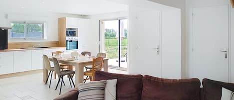 A modern kitchen with white cabinets, a dining table set for four, and a sliding glass door leading to an outdoor area.