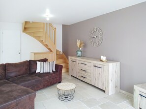 Ein Wohnzimmer mit braunem Sofa, einem Holzkabinett, einem runden Couchtisch und einer Treppe.