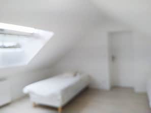 Ein Zimmer mit schrägem Dach, einem Bett und einer Tür.
