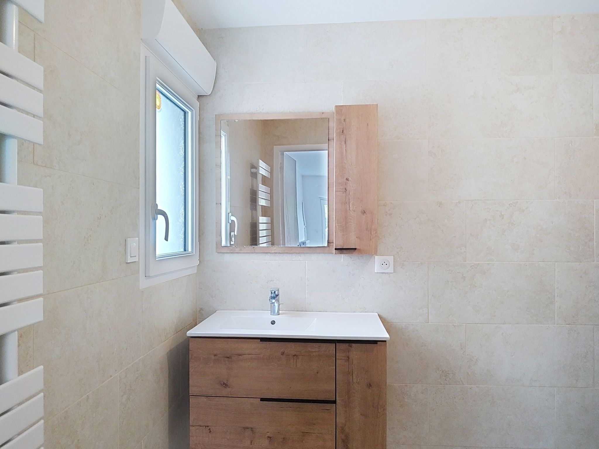 Une salle de bain avec un lavabo blanc, un meuble-lavabo en bois, un miroir et une fenêtre.