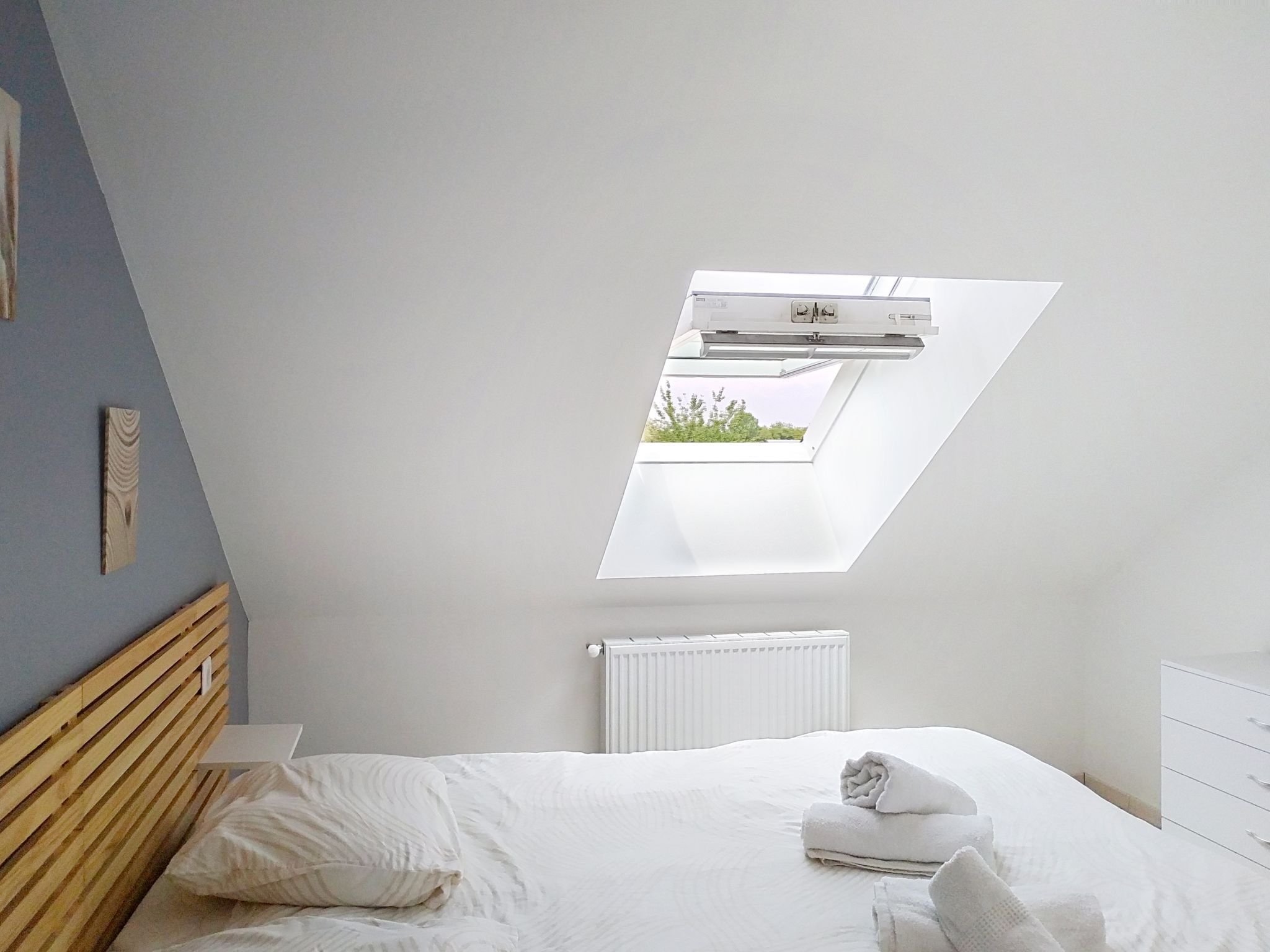 Una camera da letto con un velux, un letto, un comodino e un termosifone.