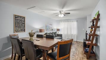 Un coin repas avec une table et des chaises en bois, un ventilateur de plafond et une étagère murale remplie de livres.