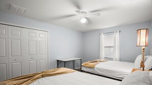 Une chambre avec deux lits, un ventilateur de plafond, une table de chevet et une fenêtre avec des stores.