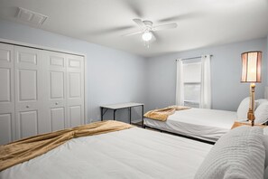 Ein Schlafzimmer mit zwei Betten, einem Deckenventilator, einem Nachttisch und einem Fenster mit Jalousien.