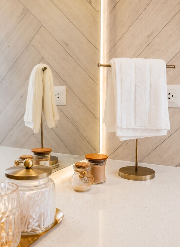 A bathroom with a wooden herringbone floor, a towel rack with white towels, and a glass jar with cotton swabs on a countertop.