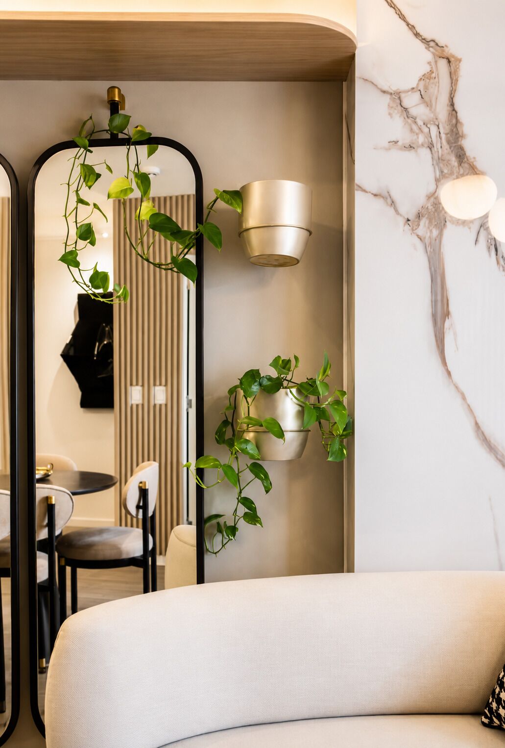 A modern bathroom with a curved white bathtub, a black-framed mirror, and a marble wall with a light fixture.