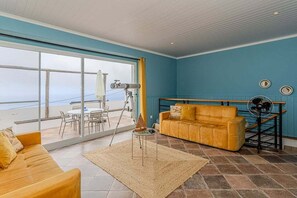 Ein Zimmer mit großem Fenster, einem gelben Sofa, einem kleinen Tisch und einem Teleskop.