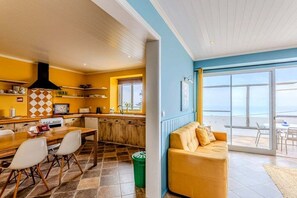 A modern kitchen with a dining area, a sofa, and a view of the sea. - GuestReady - Casa Bela Vista (Ponta Garça)