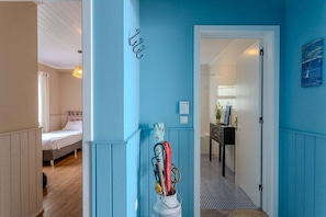 A hallway with a blue wall, a bed with white bedding, and a small table with a lamp. - GuestReady - Casa Bela Vista (Ponta Garça)