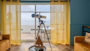 Una stanza con un telescopio su un treppiede, un tavolo rotondo con dei libri e due divani.