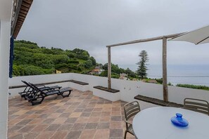 Eine Terrasse mit Tisch und Stühlen, Sonnenschirm und Blick aufs Meer.