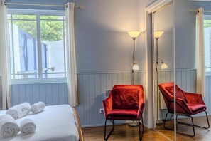Ein Zimmer mit einem Bett, zwei roten Stühlen, einem Spiegel und einem fensterbepflanzten Fenster.