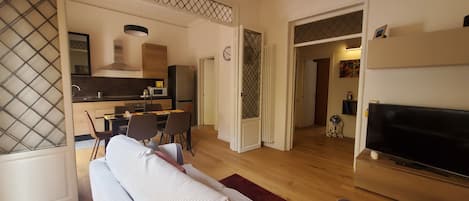 Una sala de estar moderna con sofá, un comedor con sillas y mesa, una cocina equipada y un televisor.