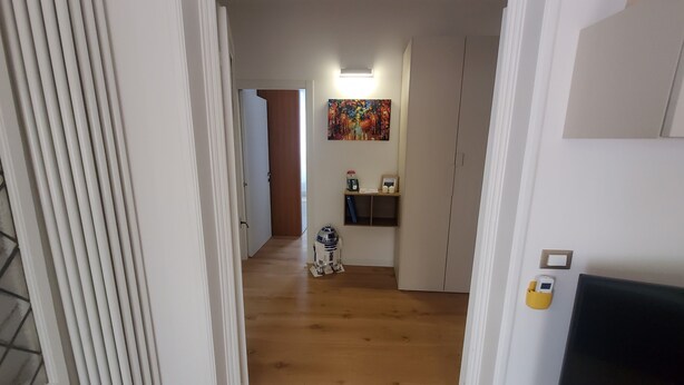 Un pasillo con piso de madera, una puerta al final y un estante con una figurita.