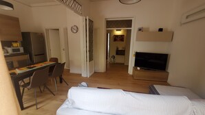 Un espacio habitable compacto con kitchenette, comedor y un dormitorio con televisor.