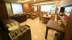 Ein Restaurant mit mehreren Tischen und Stühlen, einem Buffet mit angerichteten Speisen und Besteck sowie Blick ins Freie durch große Fenster.
