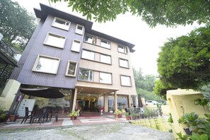 A multi-story building with a flat roof, large windows, and an outdoor seating area with chairs and potted plants. - Royal Rosette BY Rosalie (Nainital)