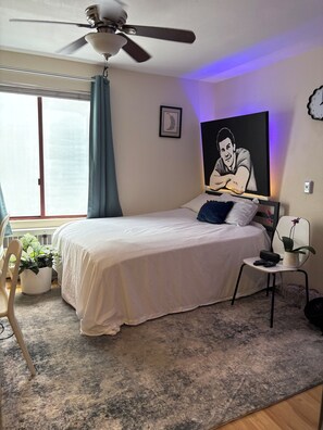 A bedroom with a bed, a ceiling fan, a window with curtains, a wall clock, and a framed picture. - Prime Location Studio near Convention Center w/ Gated Parking & Fast Wi-Fi (San Diego)