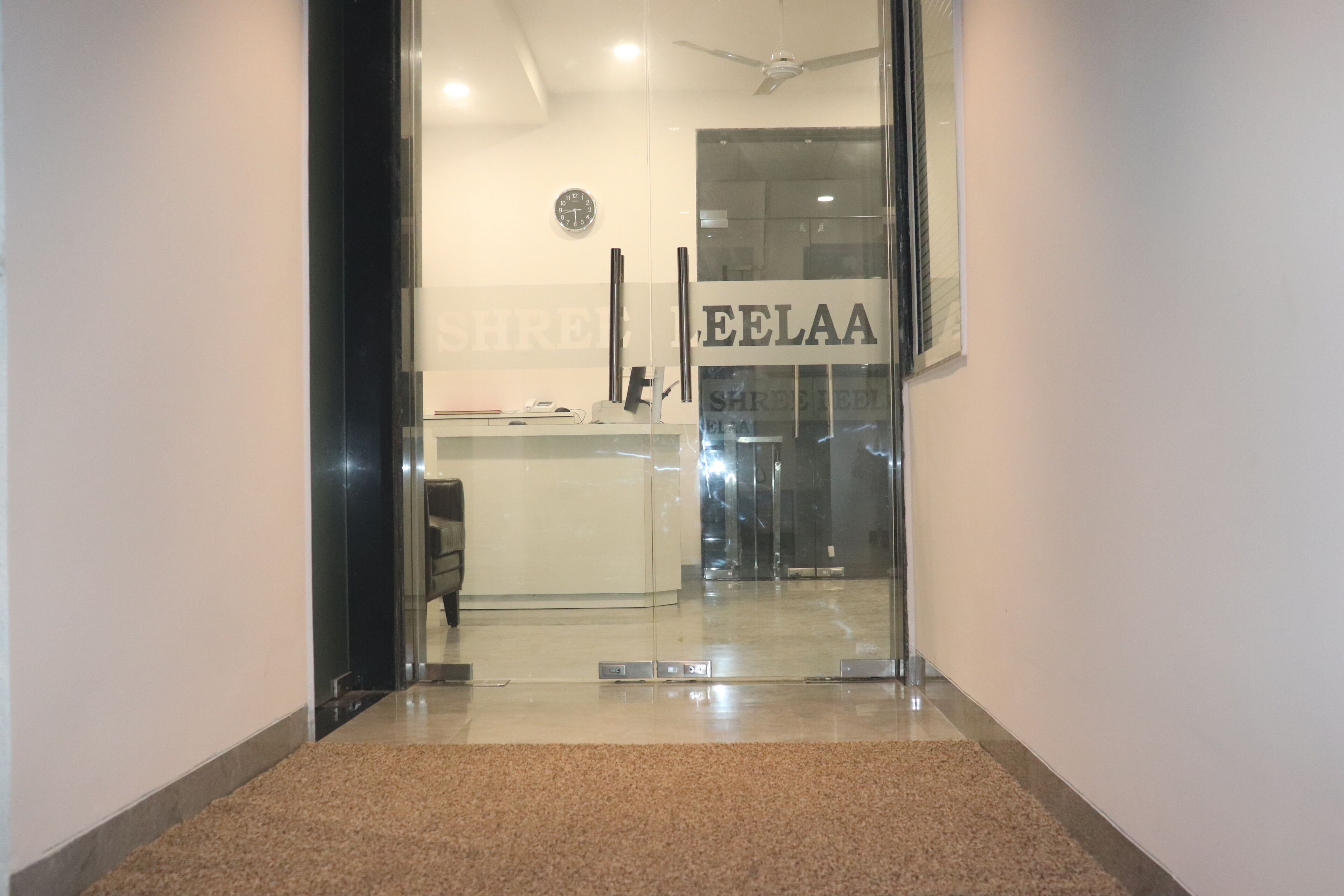 A hallway leading to a reception area with a glass door, a clock on the wall, and a sign that reads 'SHRELLA'.