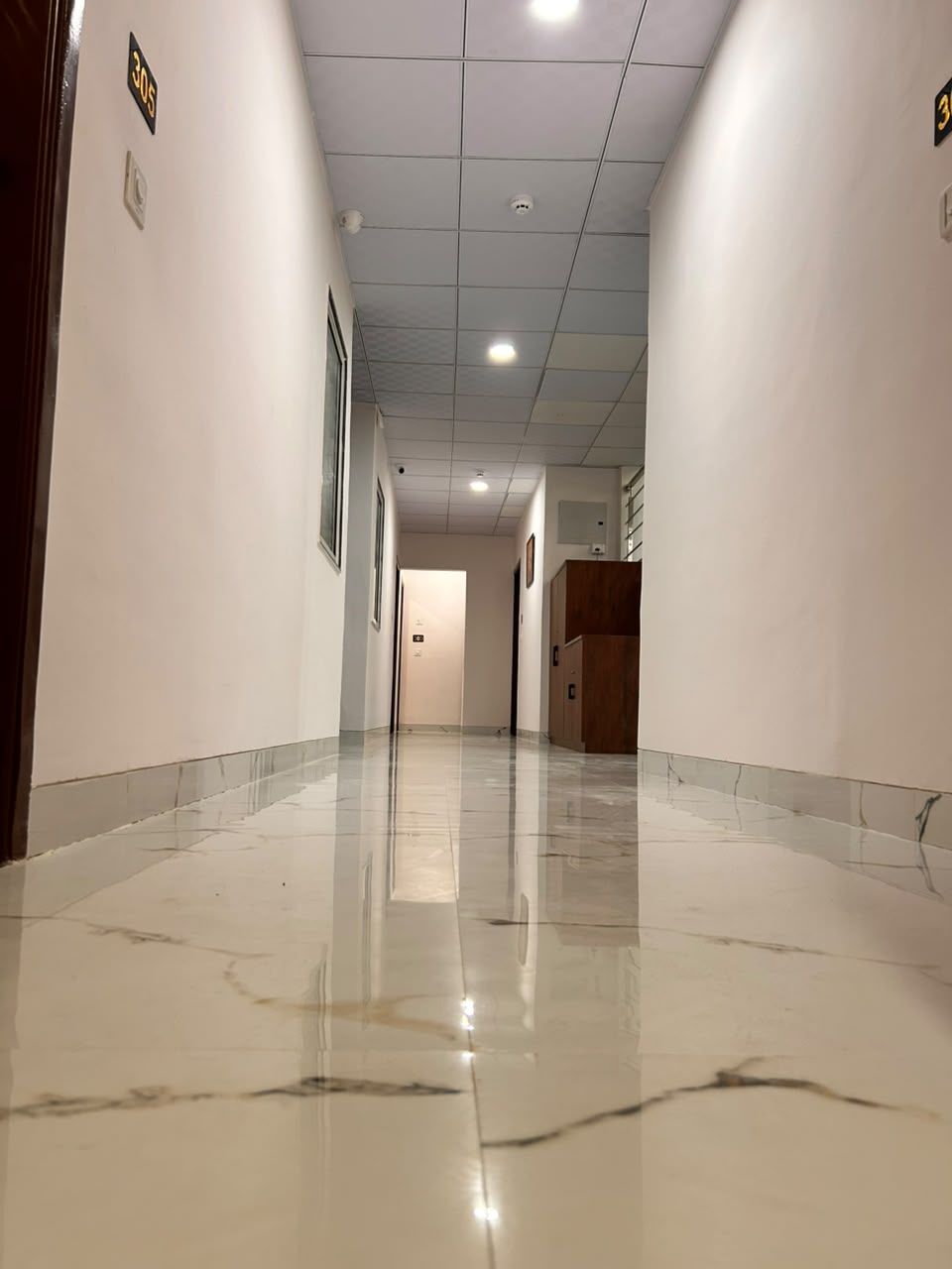 A corridor with a shiny tiled floor, white walls, and a wooden door at the end.