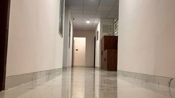 A corridor with a shiny tiled floor, white walls, and a wooden door at the end.