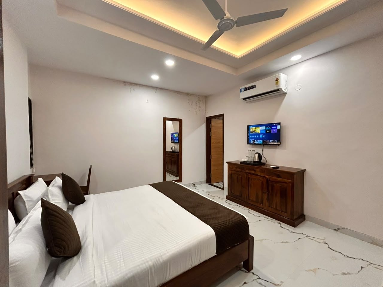 A bedroom with a bed, a wooden dresser, a television, and an air conditioning unit.