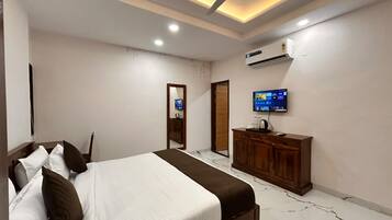 A bedroom with a bed, a wooden dresser, a television, and an air conditioning unit.