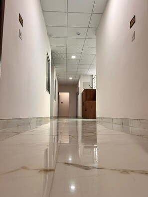A corridor with a polished floor, white walls, and a wooden cabinet. - SHREE LEELAA HOTEL (Jaipur)
