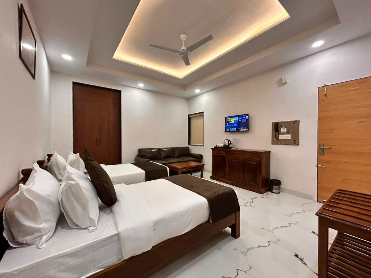 A hotel room with two beds, a sofa, a TV, a cabinet, and a wooden door.