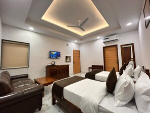 A hotel room with a bed, a sofa, a desk, a television, and an air conditioning unit. - SHREE LEELAA HOTEL (Jaipur)