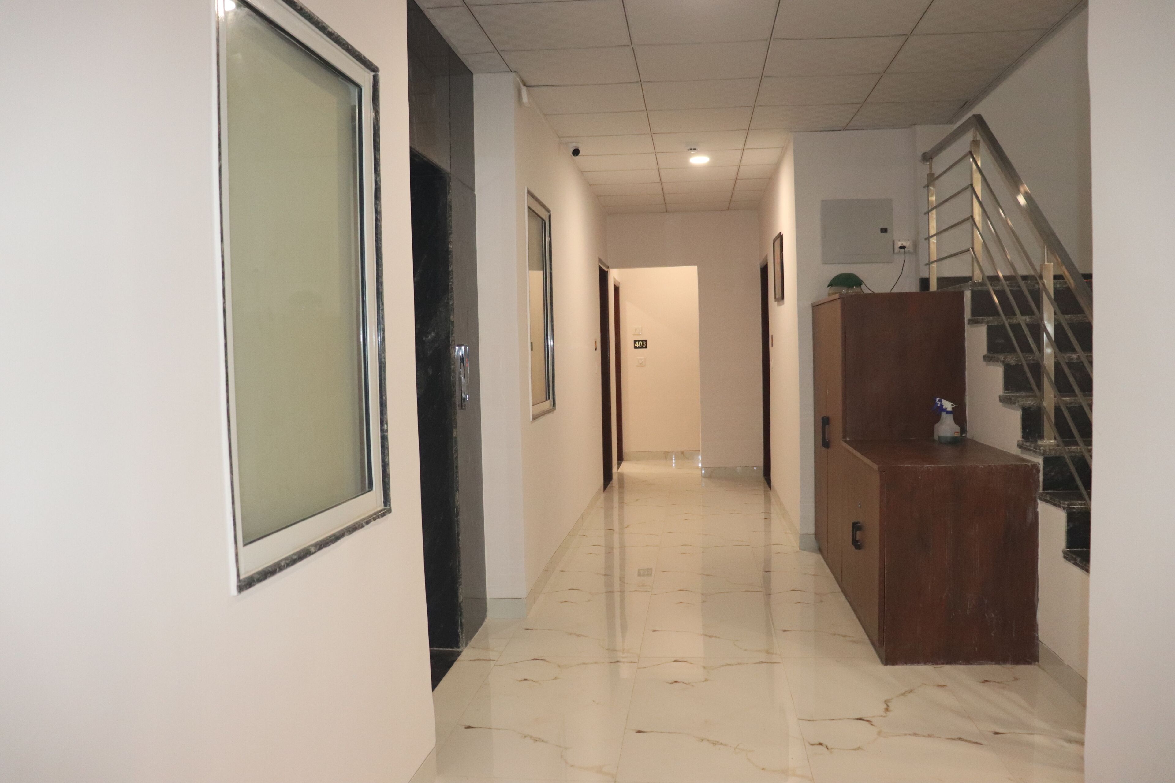A corridor with a marble floor, a wooden cabinet, and a staircase with metal railings.