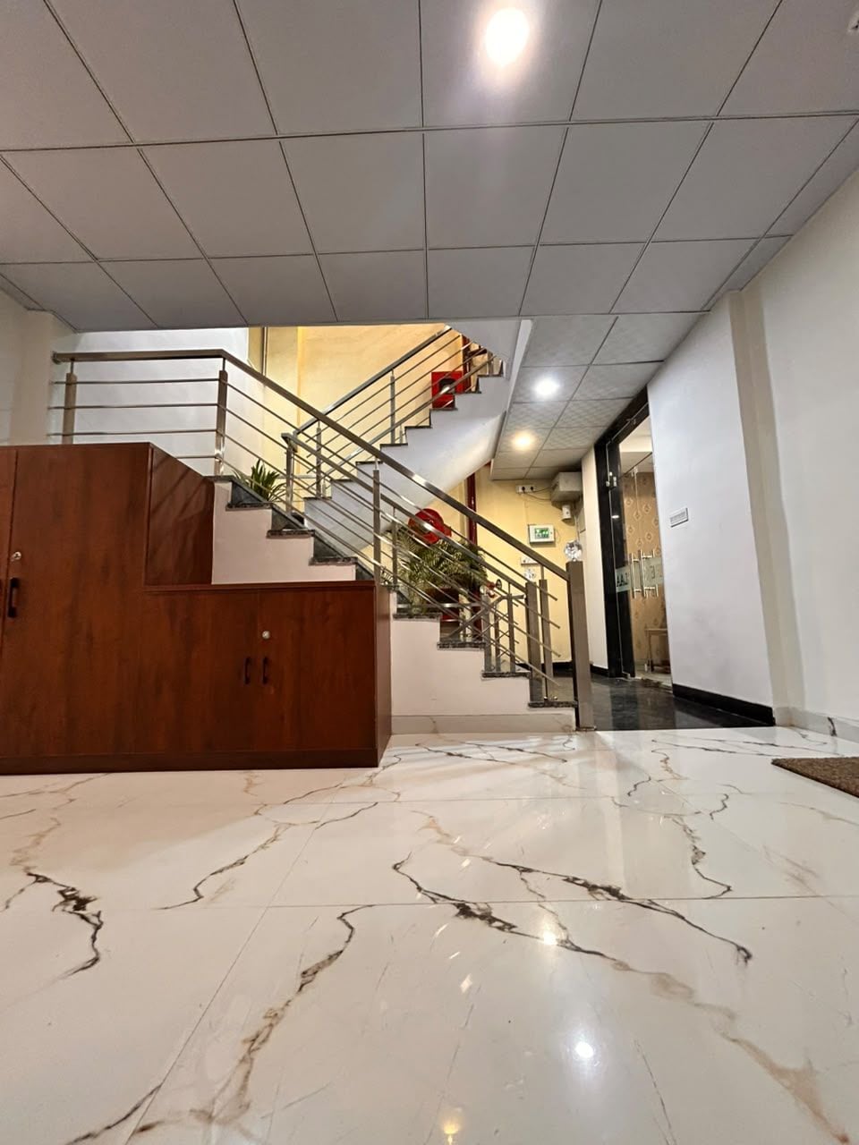 A hotel lobby with a marble floor, a staircase with metal railings, and a wooden cabinet.