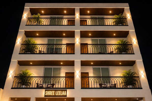Un hotel de varios pisos con balcones, cada uno con una pequeña mesa y sillas, y un letrero que dice 'SHREE LEELAA' al final.