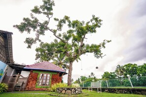 A house with a red-tiled roof, a brick exterior, and a large tree in front.