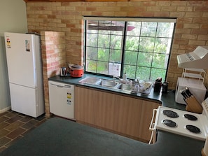 A kitchen with a brick wall, a window, a refrigerator, a dishwasher, a stove, and a sink. - Gumnut Cottage - 2BR Cottage, walk to beach and town, Linen & Wifi incl (Dunsborough)